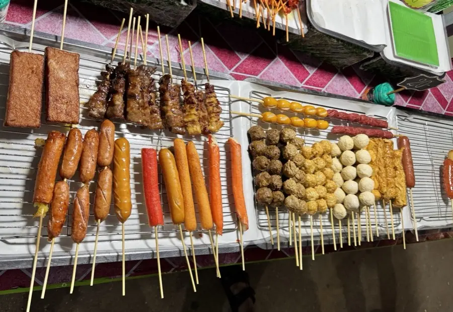 小吃摊烤架上码放整齐的各式串串:香肠、蟹柳、鱼丸、肉串
