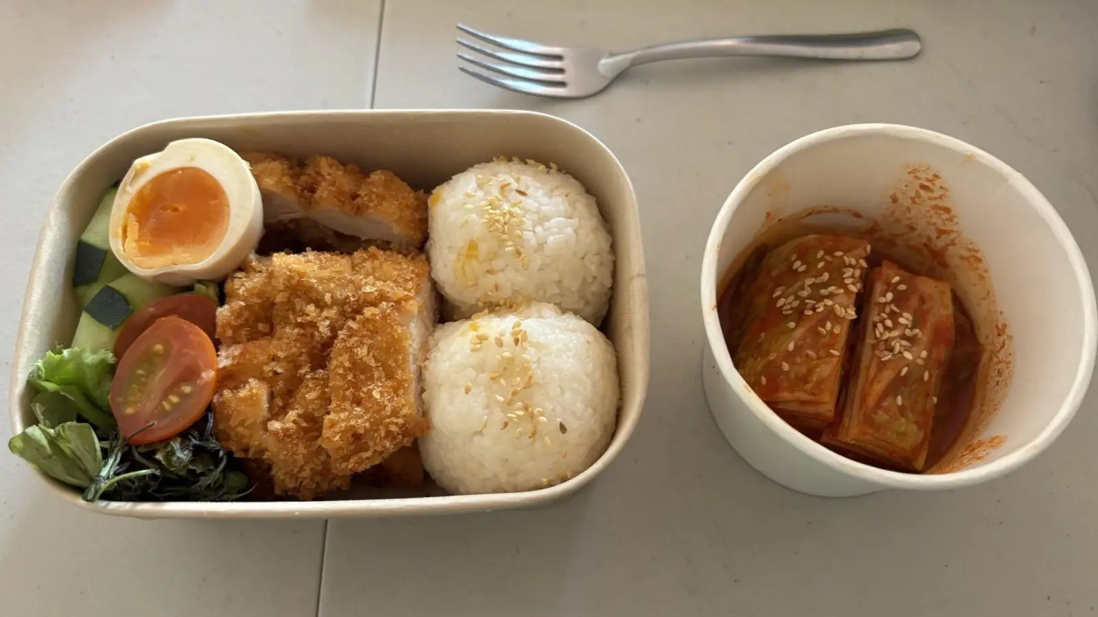 打包好的外卖餐盒:米饭、炸鸡排、溏心蛋和蔬菜,旁边一小杯泡菜
